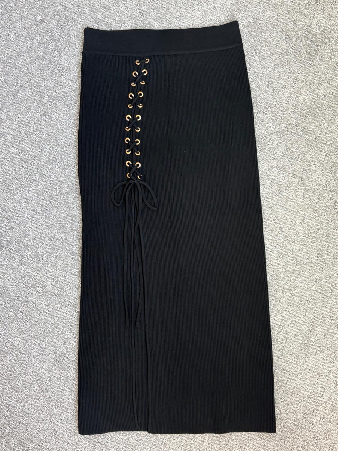 Black ribbed skirt with a side opening, featuring cord and ring details in gold, laid out over a gray rug.