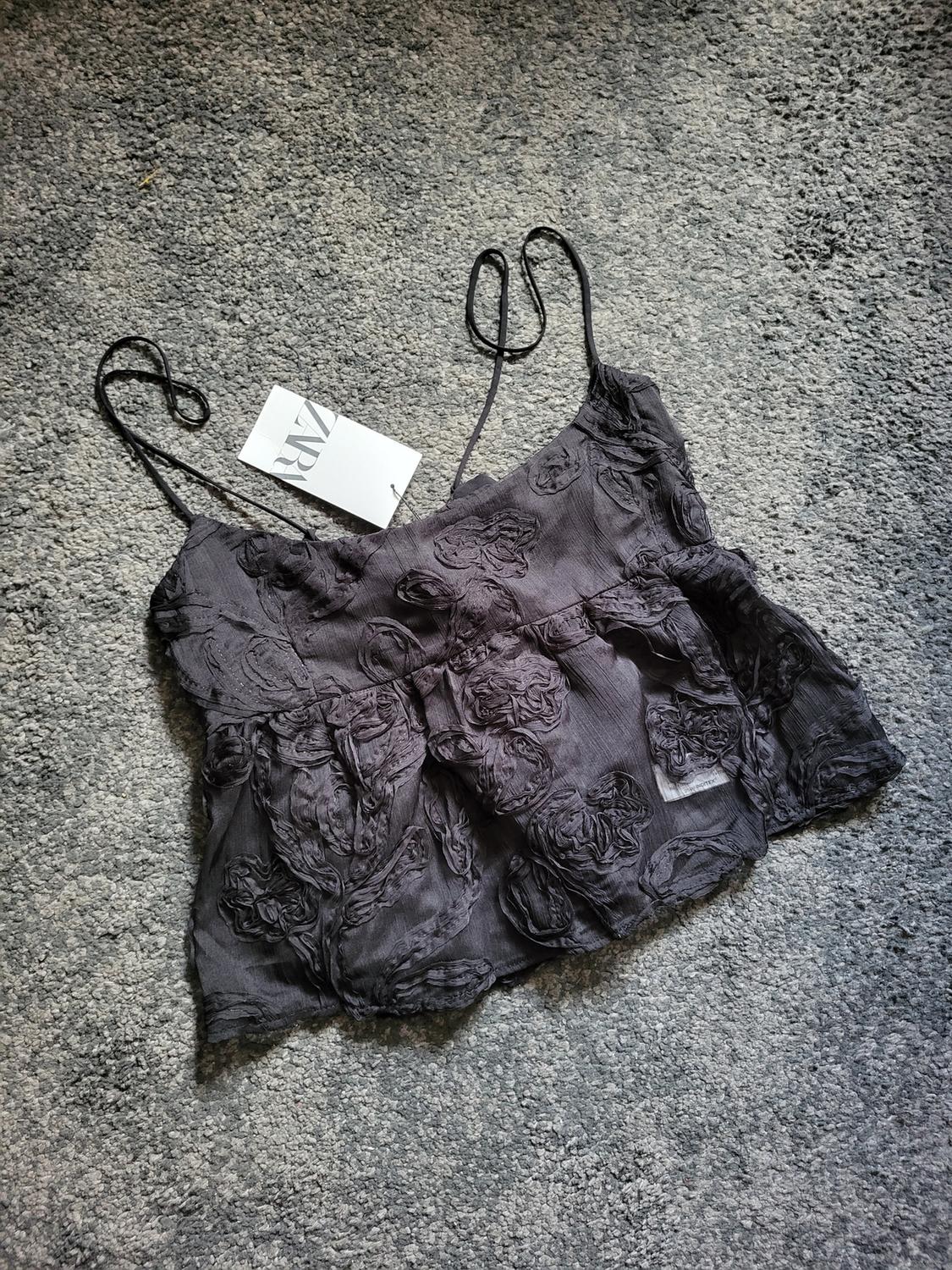 Camisole top in black fabric with floral embroidered detailing, visible label with the Zara logo, on a grey carpet.