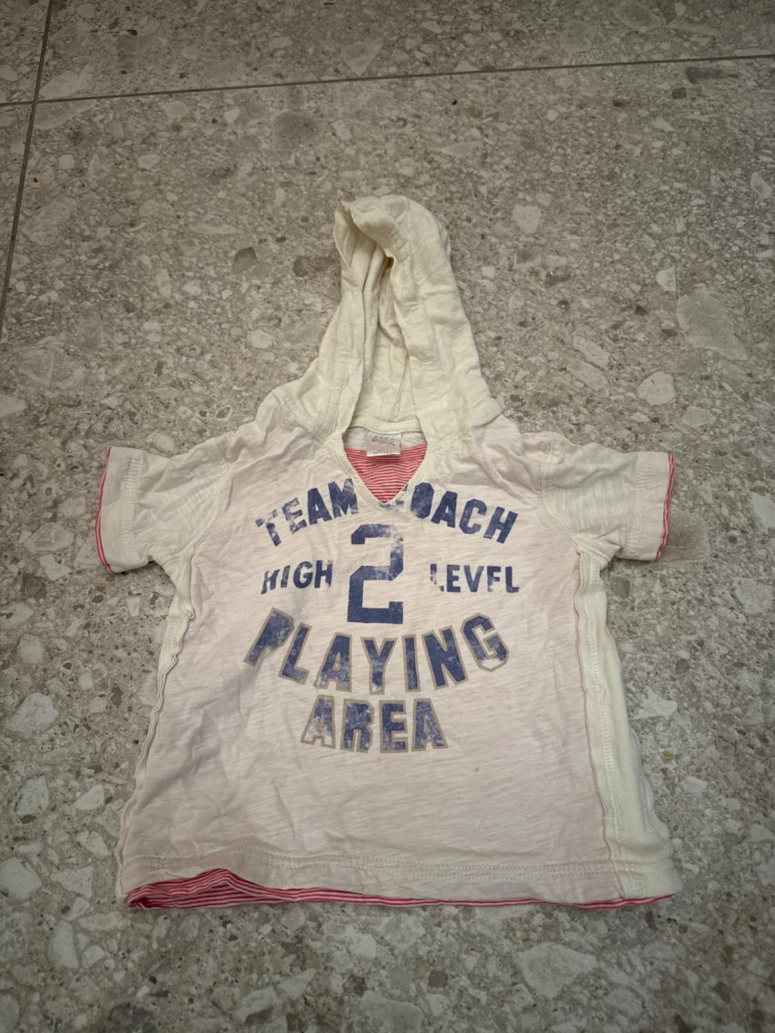 White hooded sweatshirt on a stone floor. On the front, it features the text: "TEAM ENTRENADOR HIGH LEVEL 2 PLAYING AREA". It has red details.