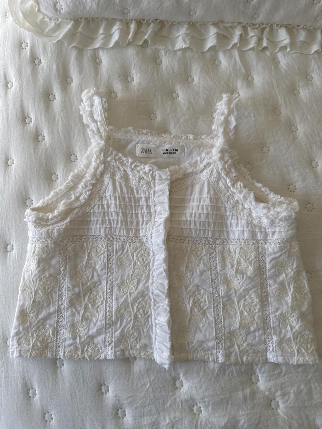 White camisole with floral embroidery on a white bedspread. Visible label: "ZARA, 6-116, MADE IN INDIA".