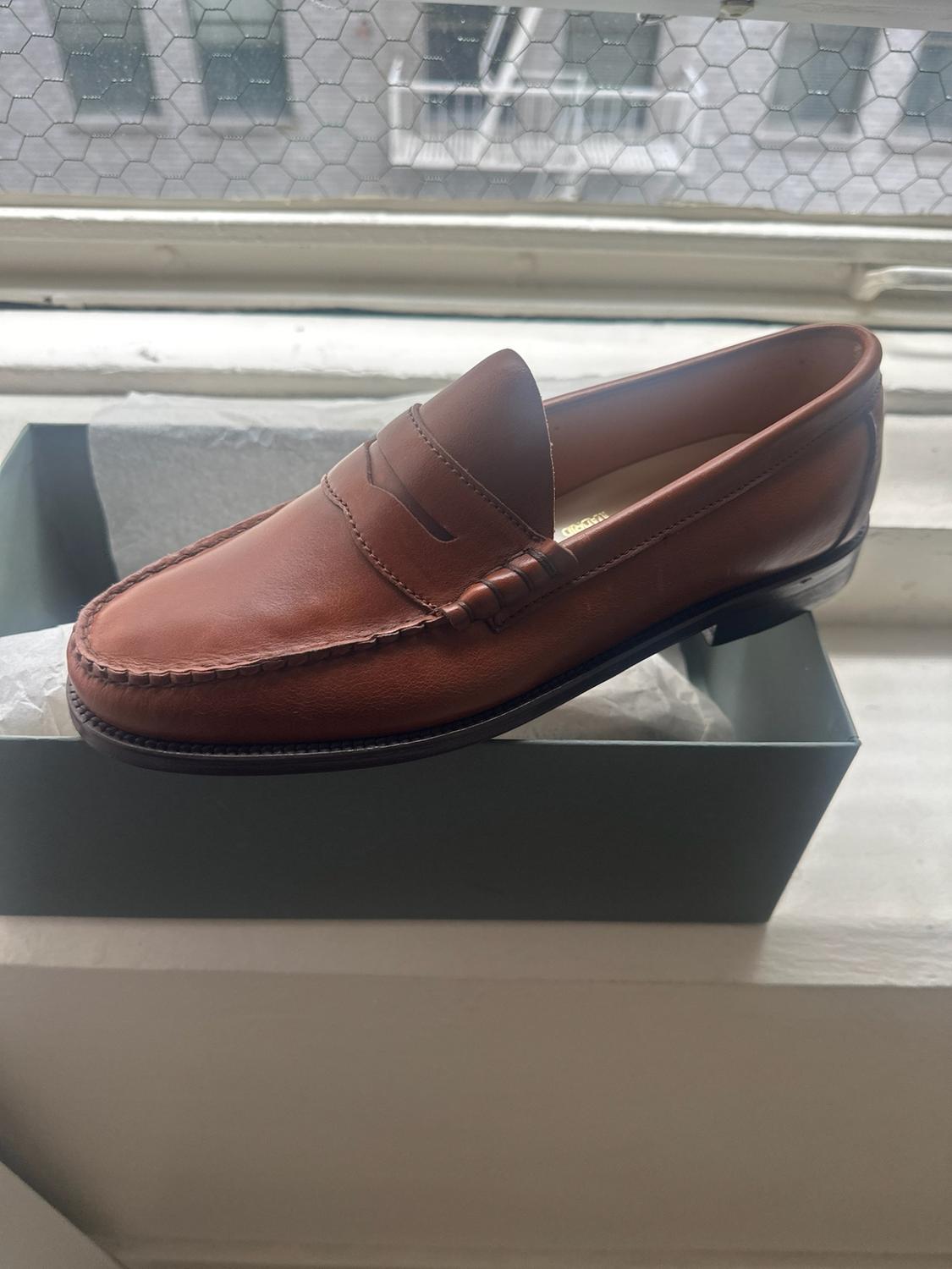 Brown leather loafer on a gray box next to a window. The inside of the shoe reads MADRID.