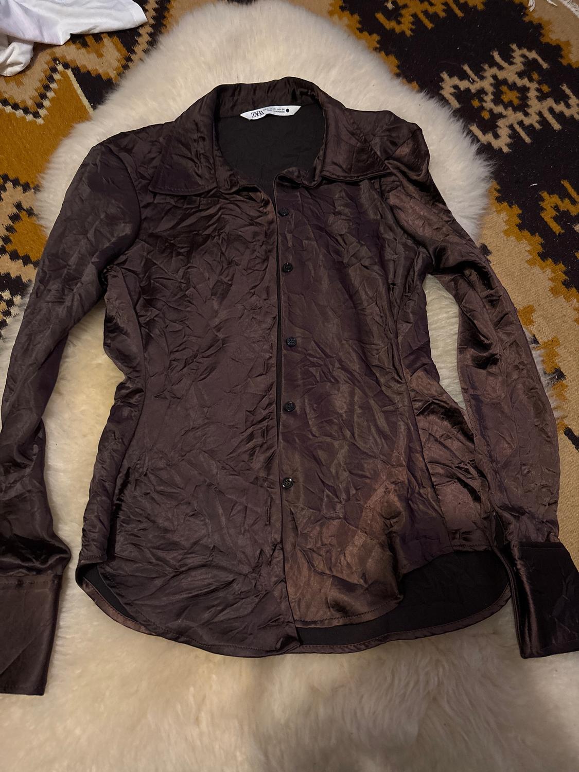 Wrinkled brown long-sleeved shirt on a geometric pattern rug with a white fur background. Visible label on the collar.