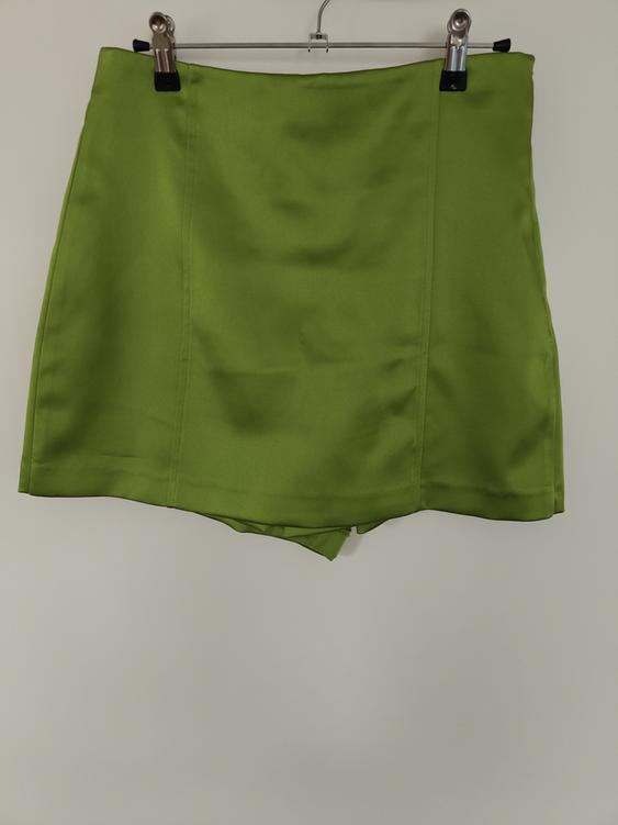 Green mini skirt hanging on a clothes hanger with clips against a white background.