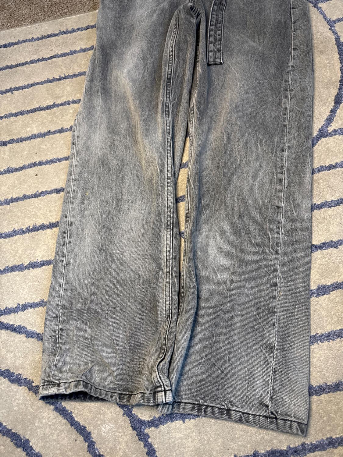 Grey loose-fit jeans on a rug with a blue line pattern. Casual style and relaxed composition.