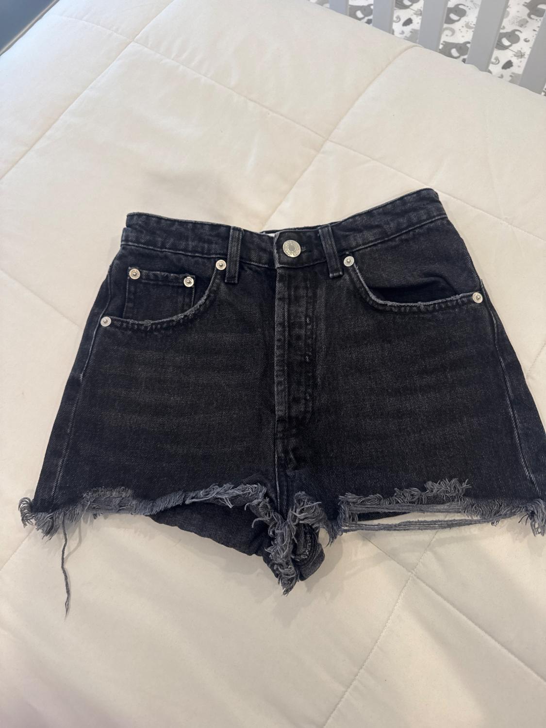 Black denim shorts with frayed edges, on a white quilted bedspread. Background with a crib design.