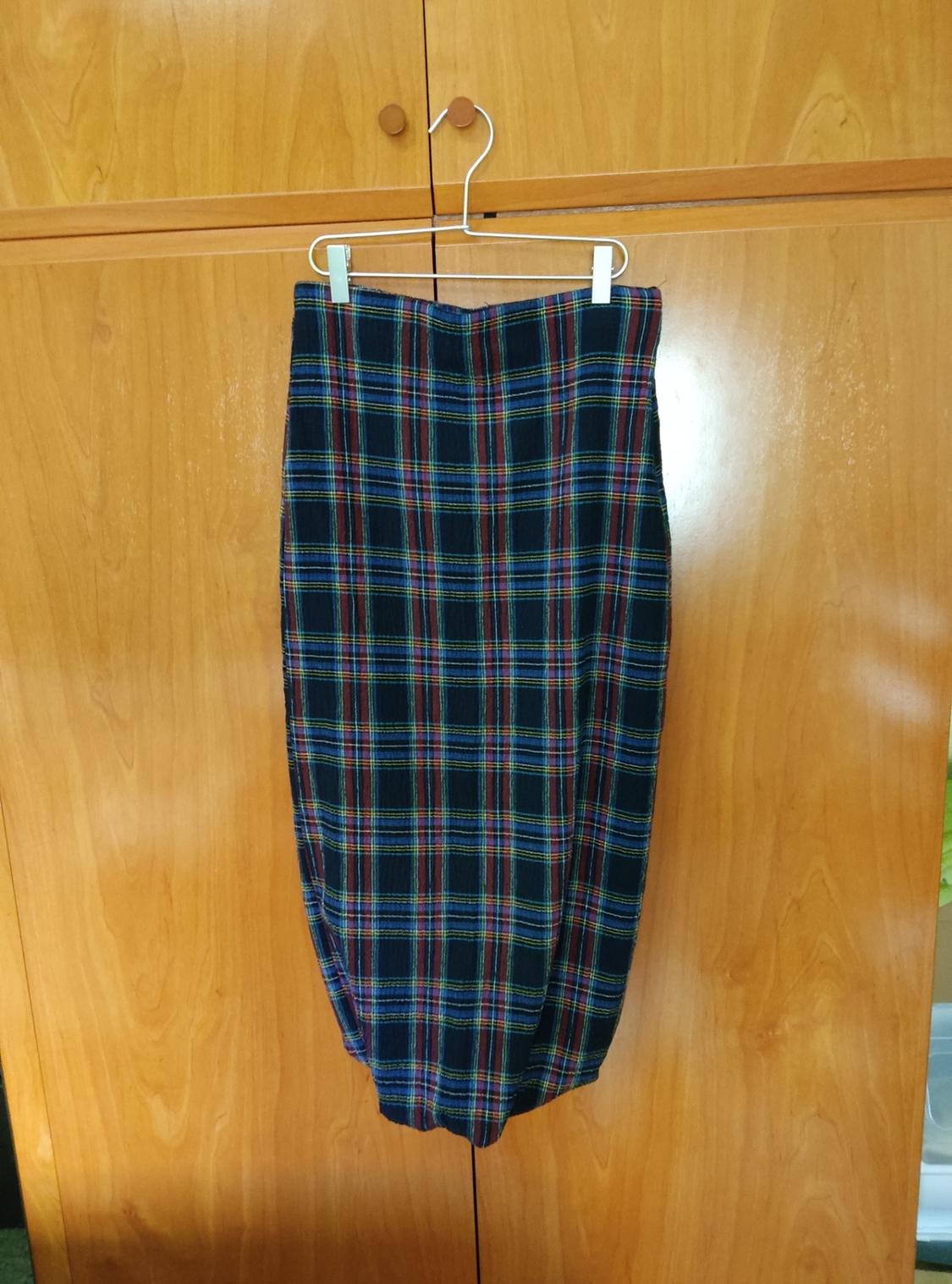 Tartan skirt in blue, red, and yellow hues hanging on a hanger in front of a light wood wardrobe.