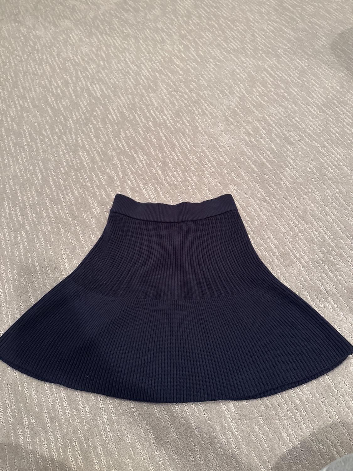 Black knitted flared skirt on a textured beige rug.