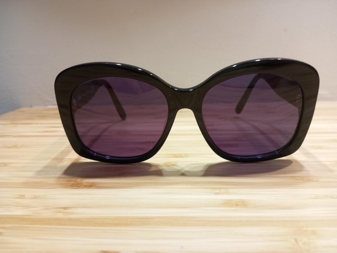 Black-framed sunglasses with dark lenses on a light wooden surface.