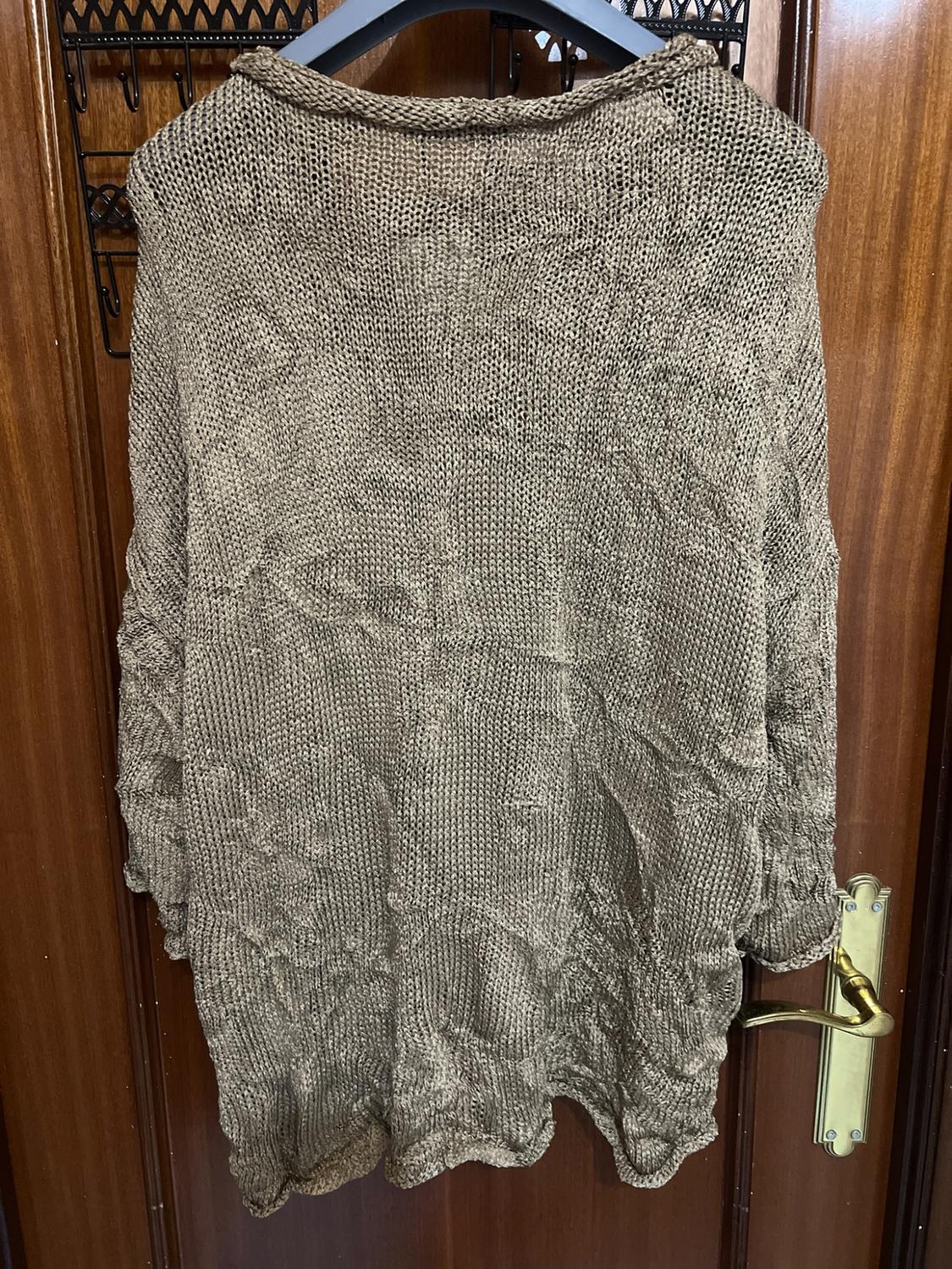 Open-knit jumper in light brown, hanging on a black hanger on a wooden door.