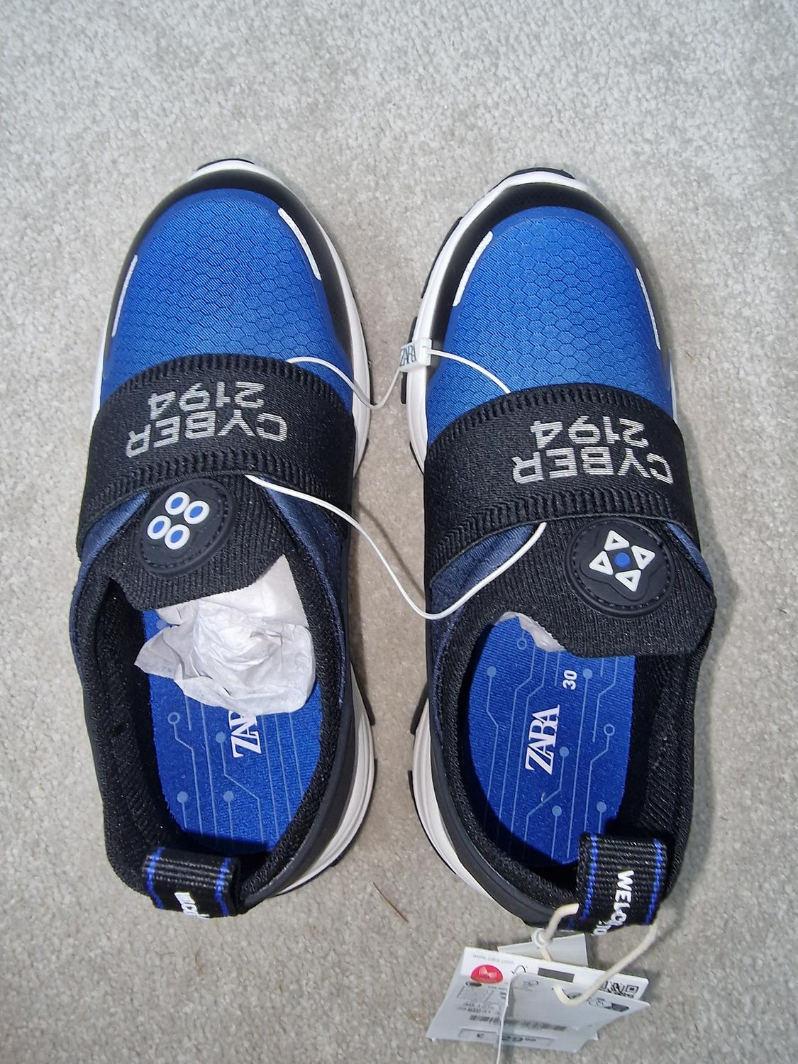 Blue trainers with black detailing and a white sole. Visible text: "CYBER 2194", "ZARA". Hanging tags present.