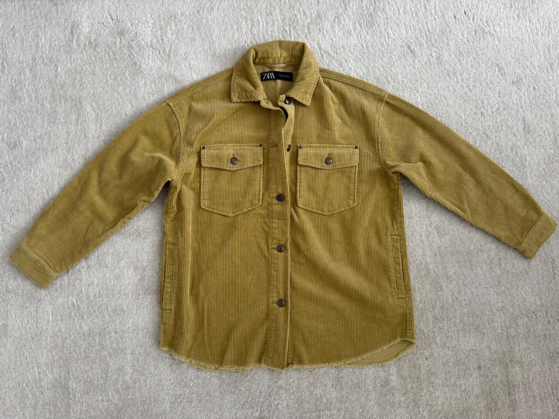 Beige corduroy shirt with two front pockets and brown buttons, laid flat on a light surface.