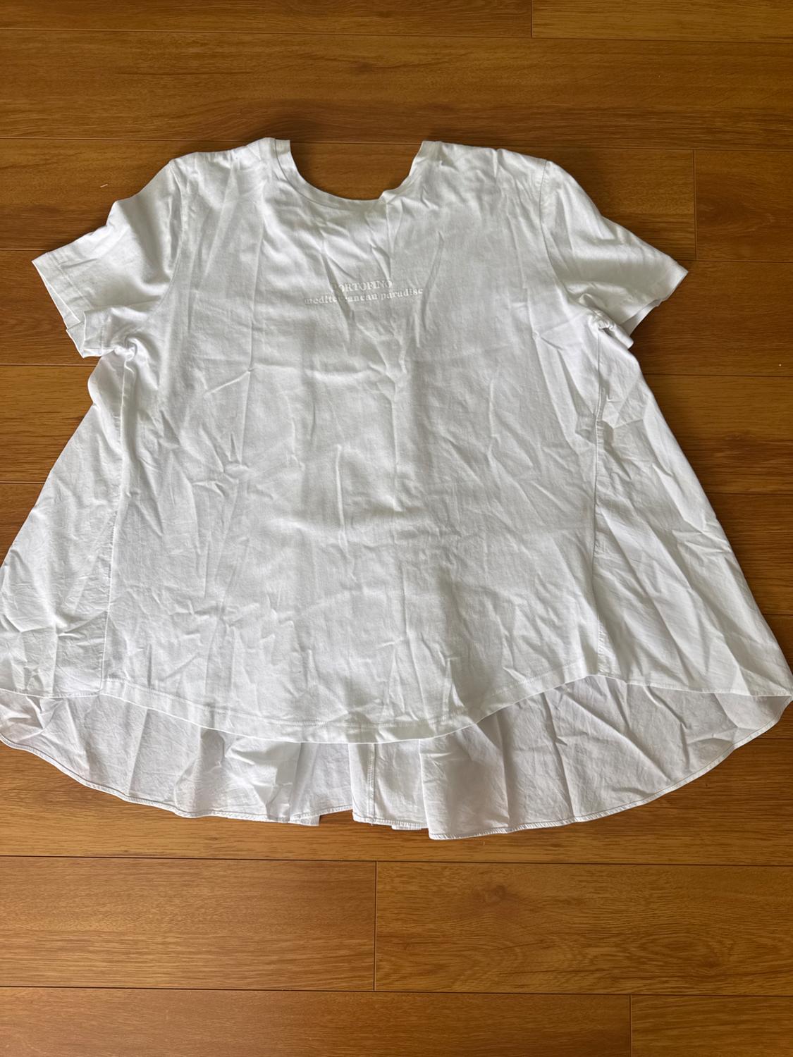 White short-sleeved T-shirt with "tropical urban paradise" text on the chest, on a wooden floor.