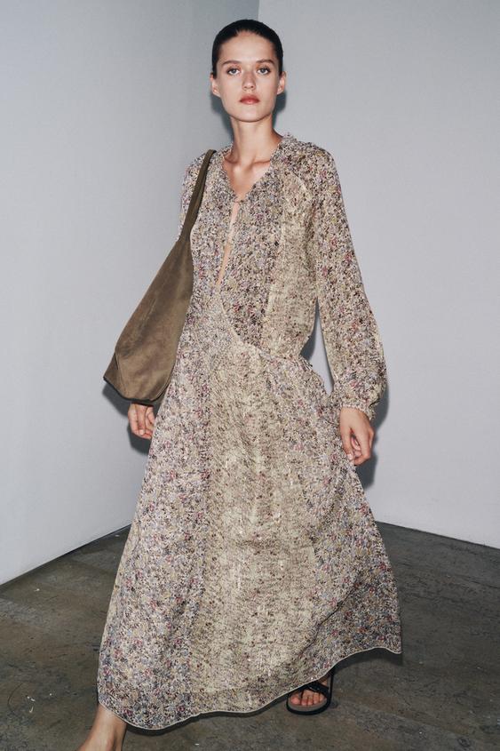 Komplet dlouhých šatů s květinovým potiskem, výstřihem do V a dlouhými rukávy, hnědá kabelka přes rameno.