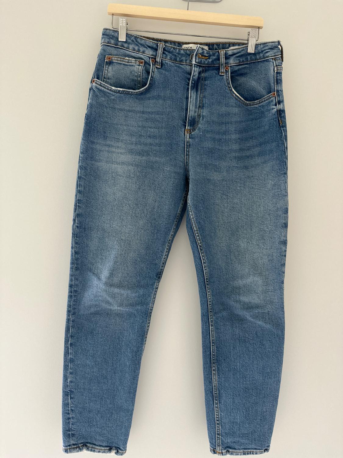 Blue jeans hung on a wooden hanger on a white background. Classic design with five pockets and button closure.