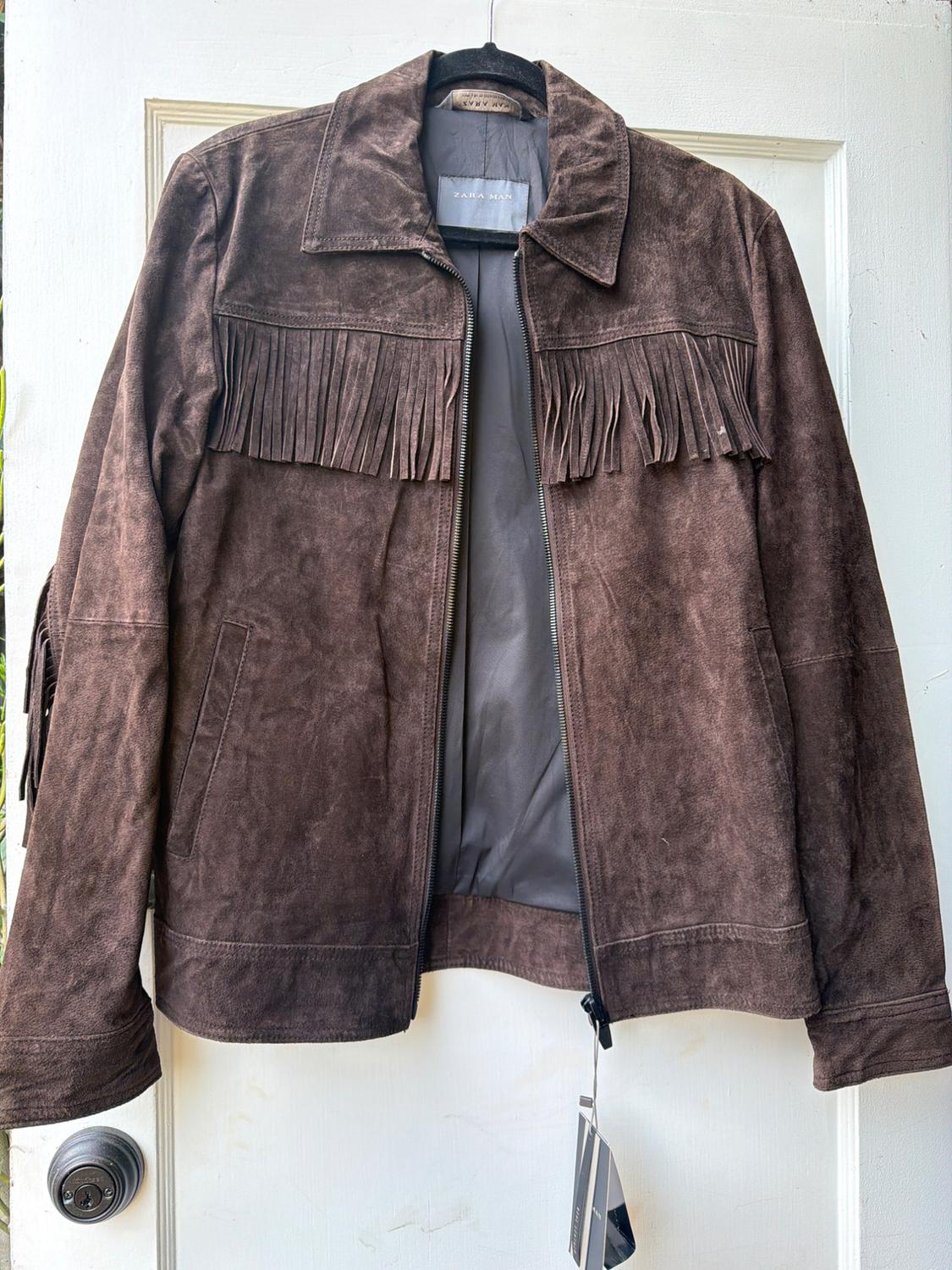 Brown suede jacket with fringe and a zipper, hanging on a white door. The text ZARA MAN can be read on the inner label.
