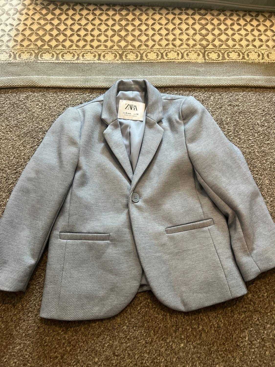 Grey textured children's blazer on a carpet. Visible label with the text ZARA SIZE 6 YEARS cm 116 MADE IN TURKEY.