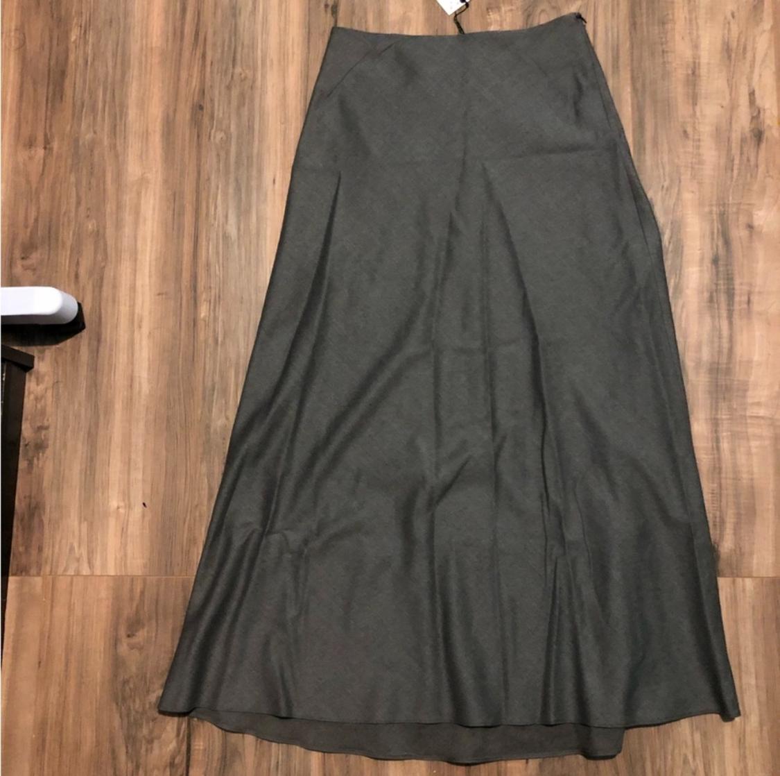 Gray long skirt on a wooden floor. The fabric has a slight sheen and visible pleats. Hangtag at the top.