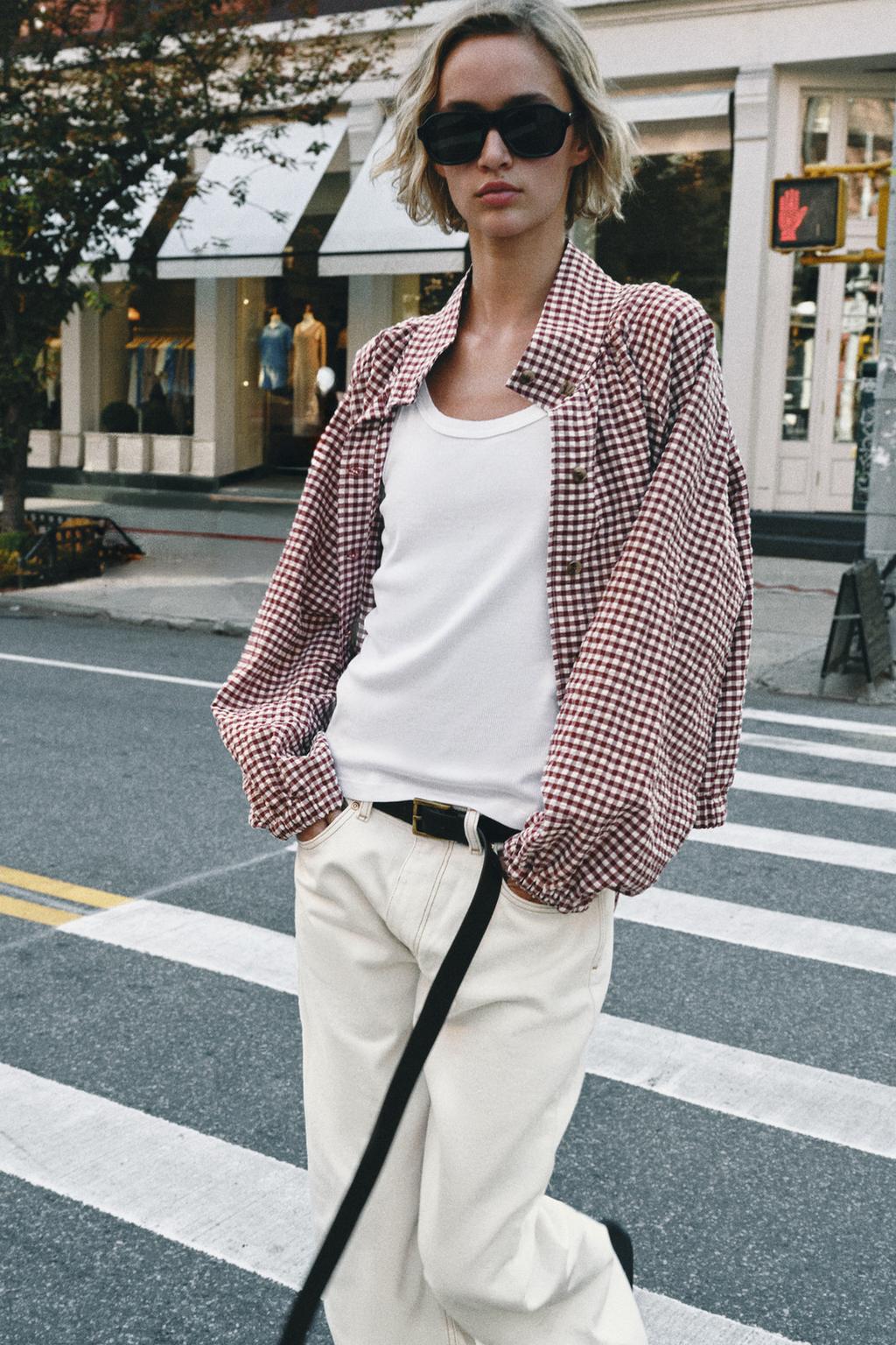 Conjunto de cazadora de cuadros granate y crudo con mangas anchas, camiseta blanca, pantalón crudo con bolsillos laterales y cinturón negro.