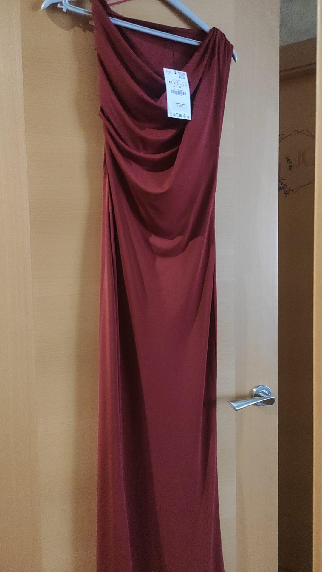 Long maroon dress with a draped neckline hanging on a light wood door. It has a white label at the top.