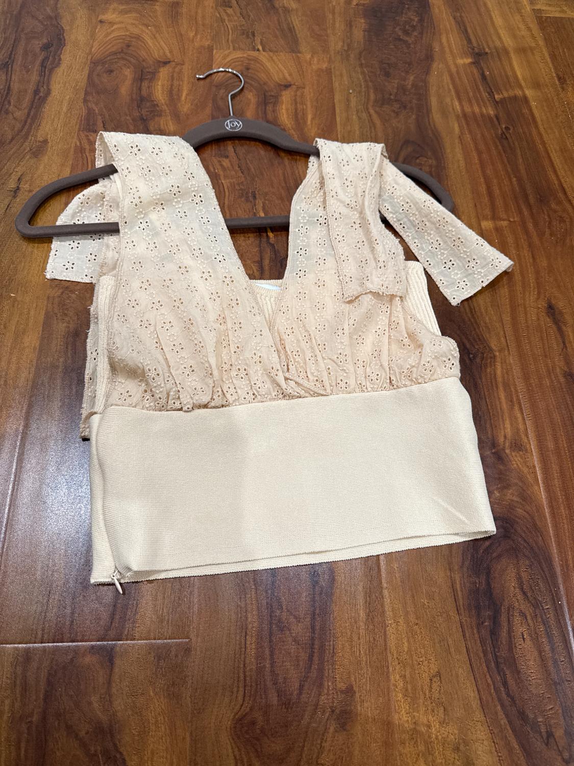 Beige lace blouse with short sleeves, hanging on a hanger over a brown wooden floor.