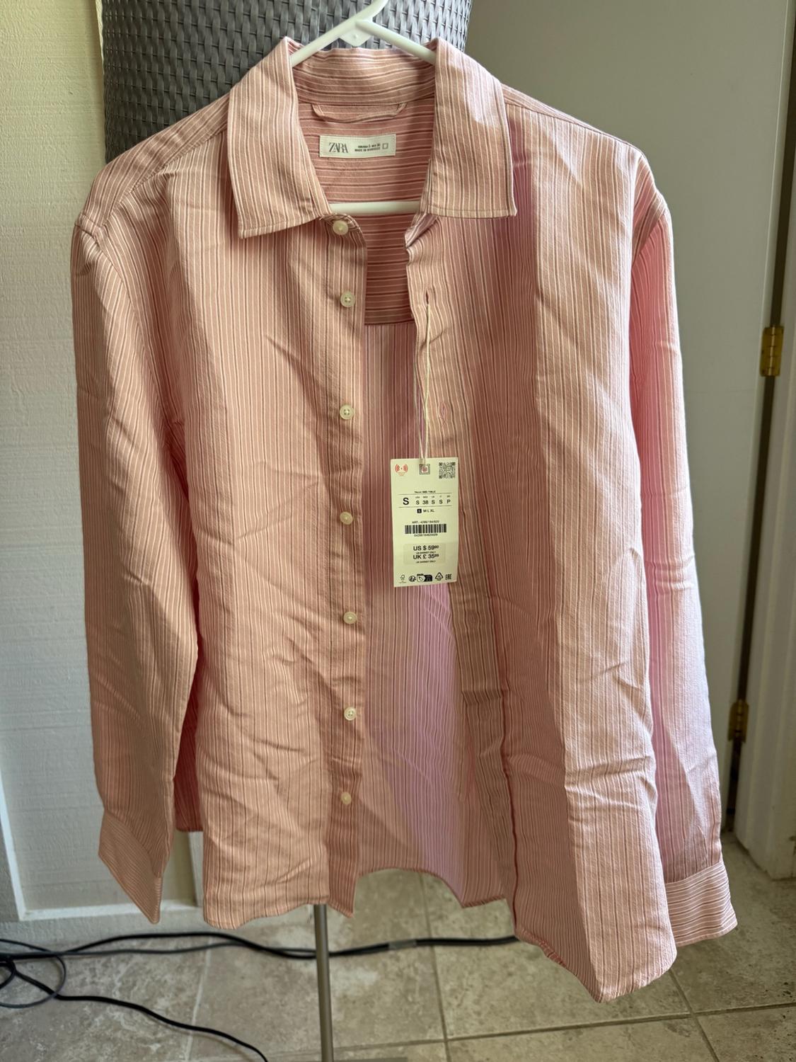 Pink long-sleeved shirt with white stripes hanging on a hanger. Label with ZARA text on the collar and a price tag.