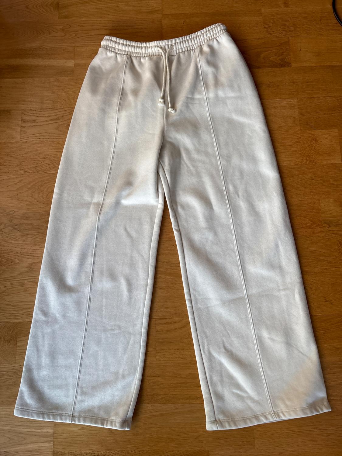 White, wide-leg trousers with an elasticated drawstring waist, on a light wooden floor.