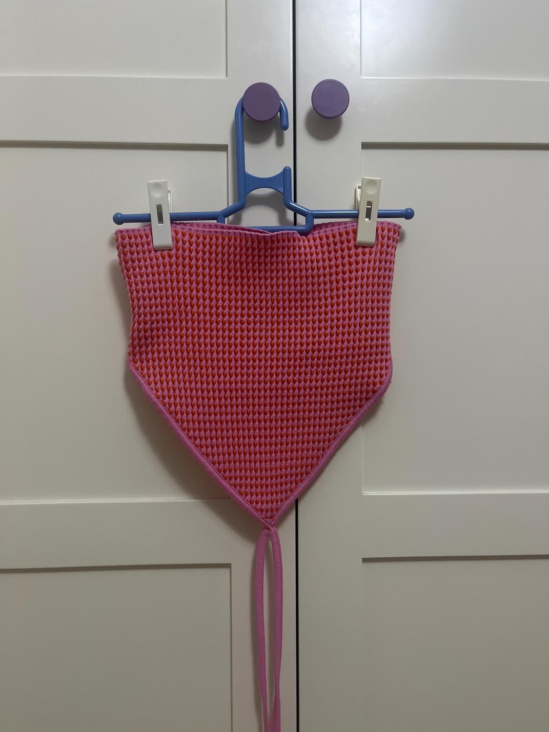 Pink knitted top hanging on a blue hanger with white pegs, on a white wardrobe with purple handles.
