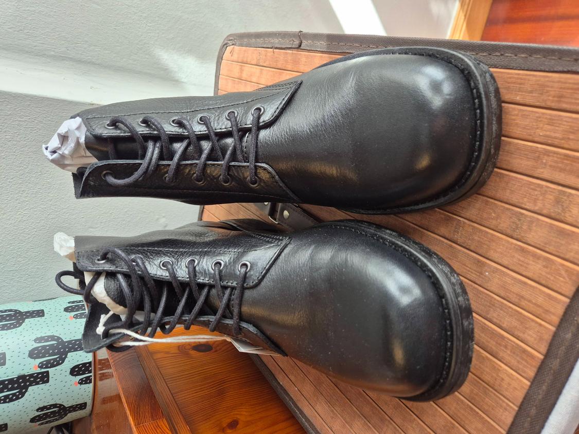 Black lace-up leather boots on a wooden slat surface, next to an object with a cactus print.