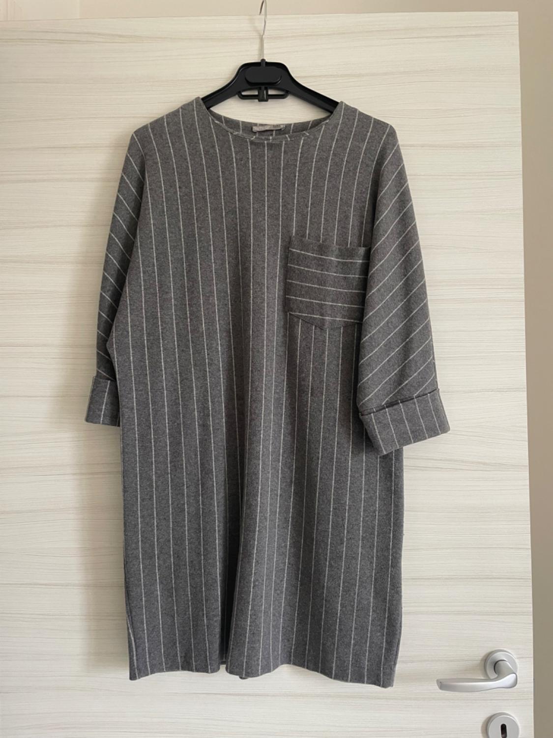 White vertically striped grey dress with a chest pocket, hanging on a black hanger over a white door.