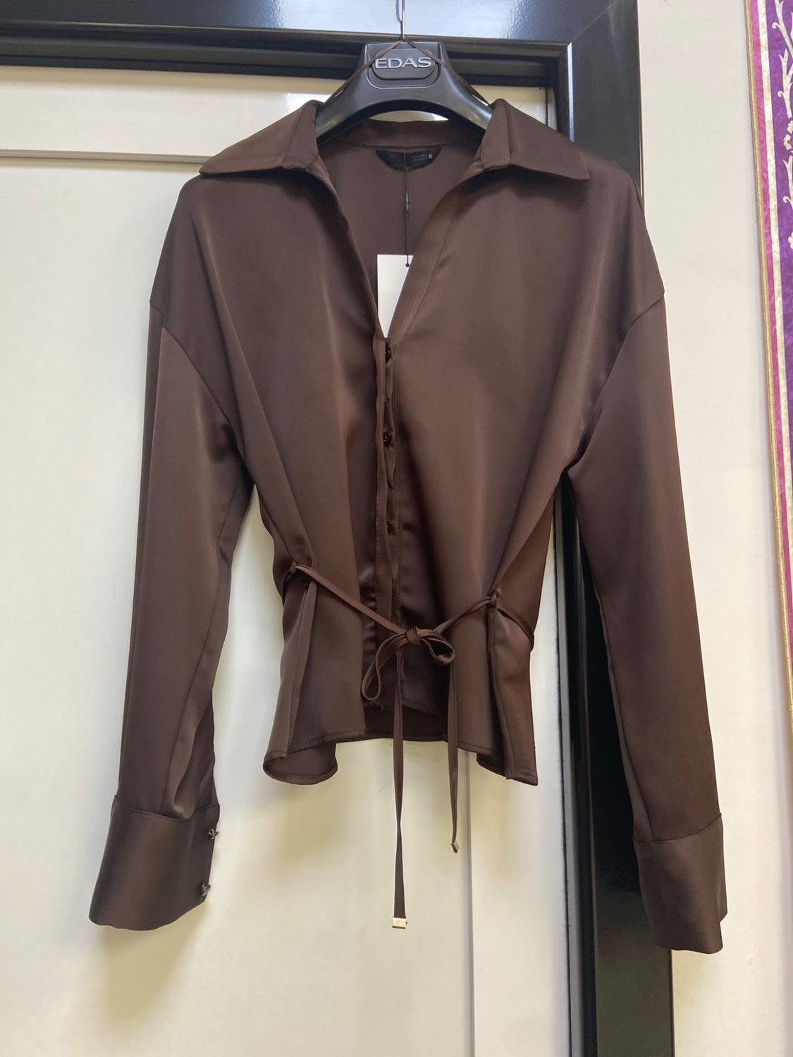 Long-sleeved satin brown blouse, buttons and tie at the waist, hanging on a black hanger with the text EDAS.