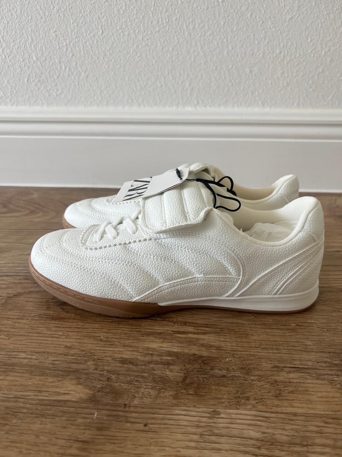 Rough-textured white sneakers with light brown soles on a wooden floor. Visible label with "ZARA" text.