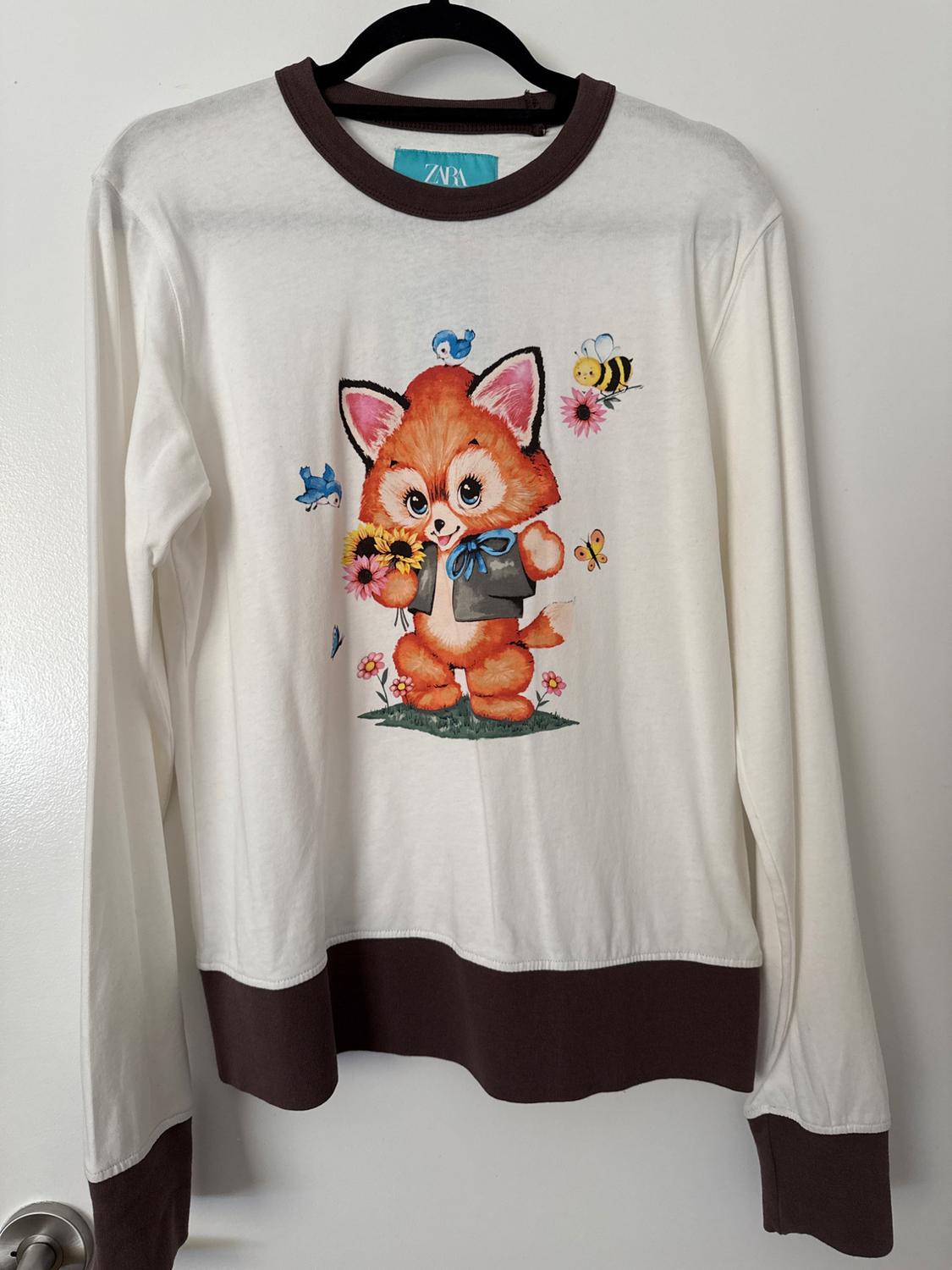 White long-sleeved T-shirt featuring brown collar, cuffs and hem. Central fox and floral print with a ZARA label at the neck.