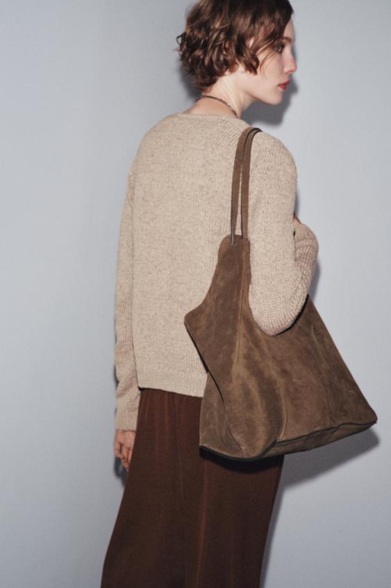 Polodetail velkého hnědého kabelky s dlouhými uchy, v kombinaci s béžovým svetrem a hnědou sukní.