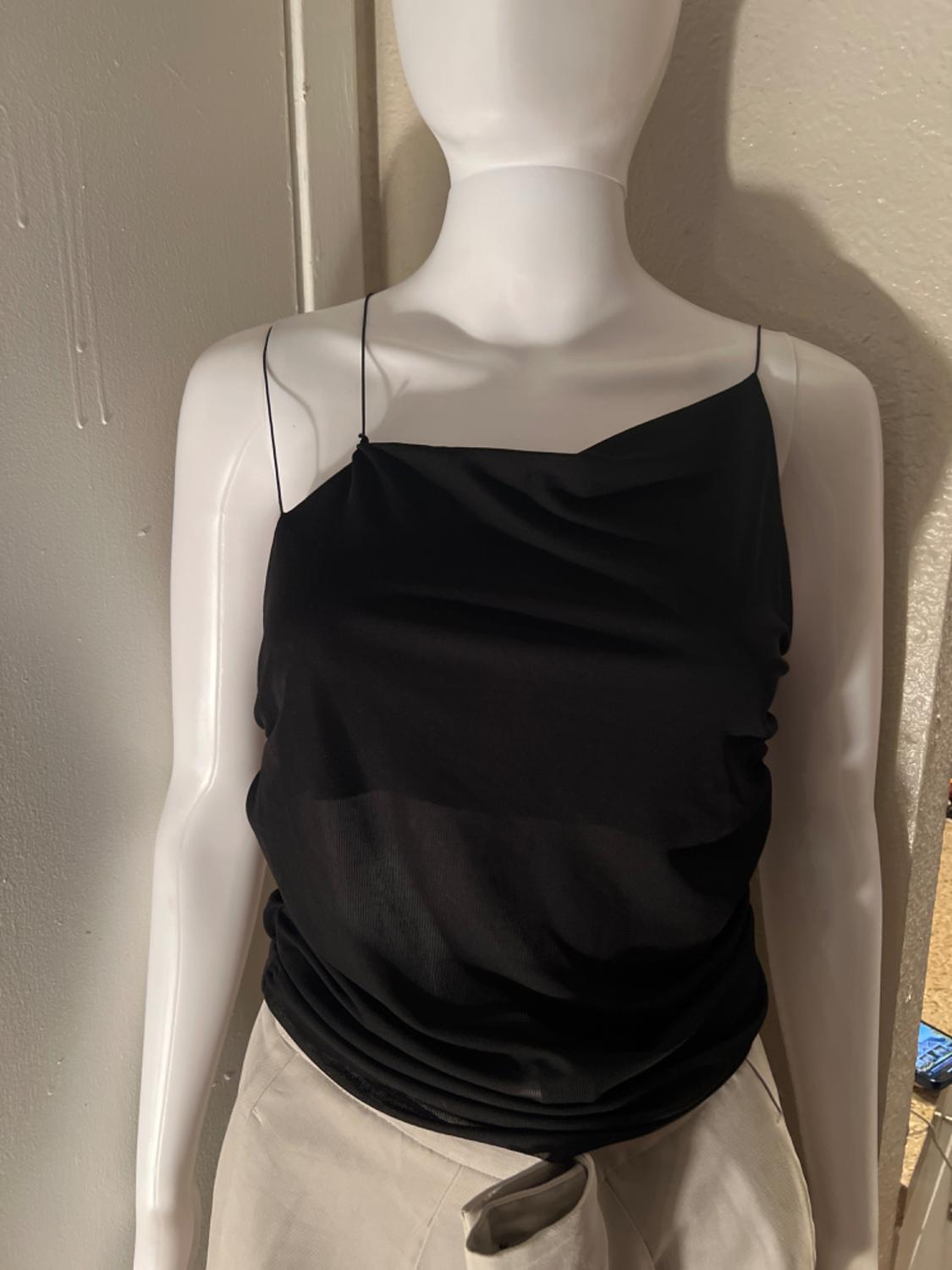 Medium shot of a black camisole top with thin straps and draping, paired with light-coloured trousers.