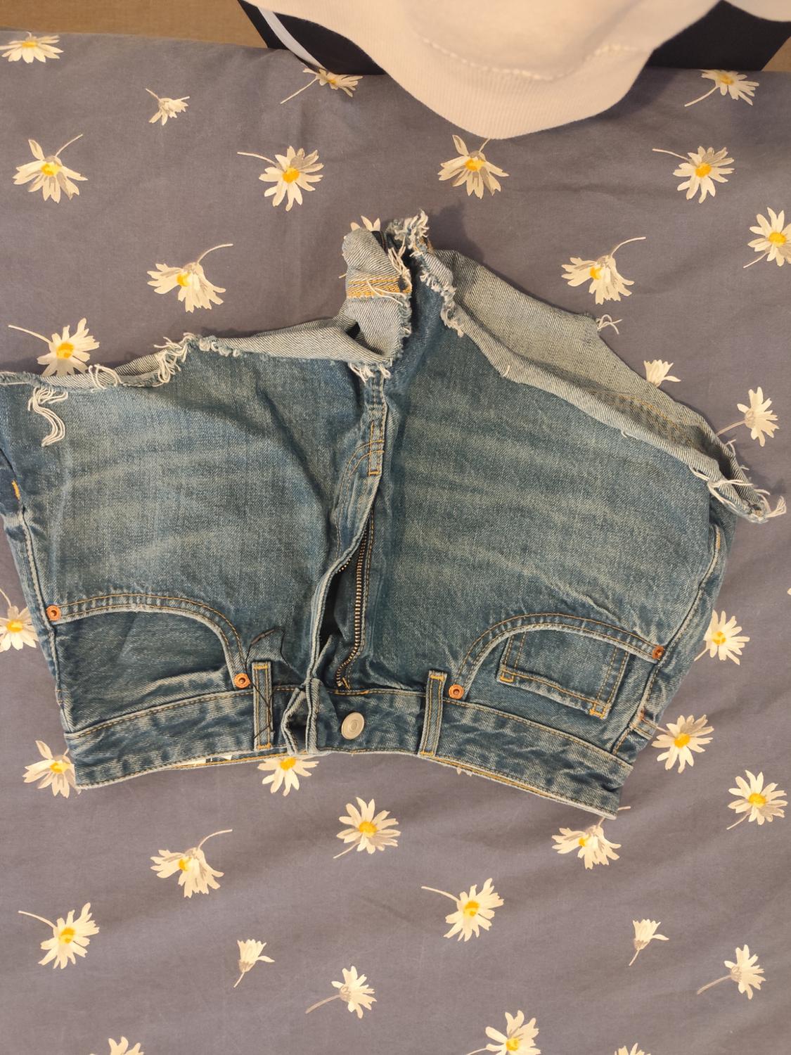 Distressed denim shorts over a blue fabric with white and yellow daisy print.