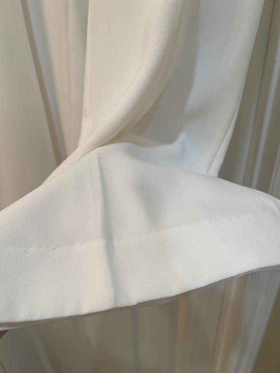 Soft, flowing white fabric with pleats, captured up close. The texture and drapery are clearly visible.
