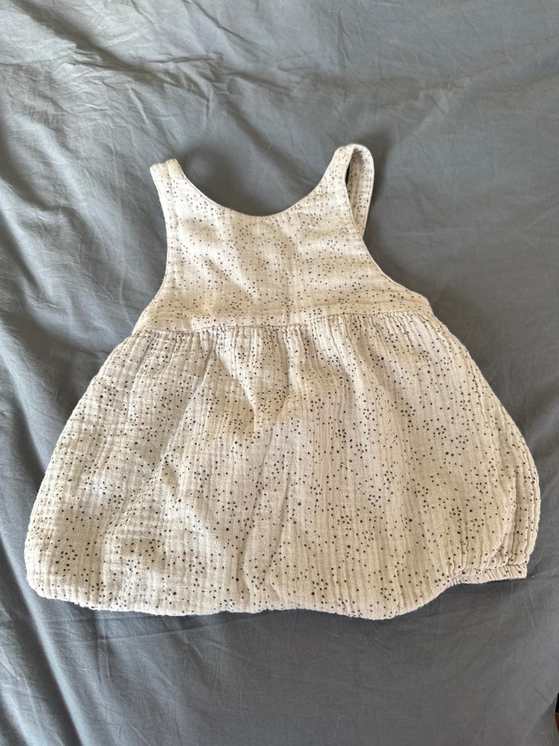 Sleeveless children's dress, light in colour with a black polka dot print, on a wrinkled grey surface.