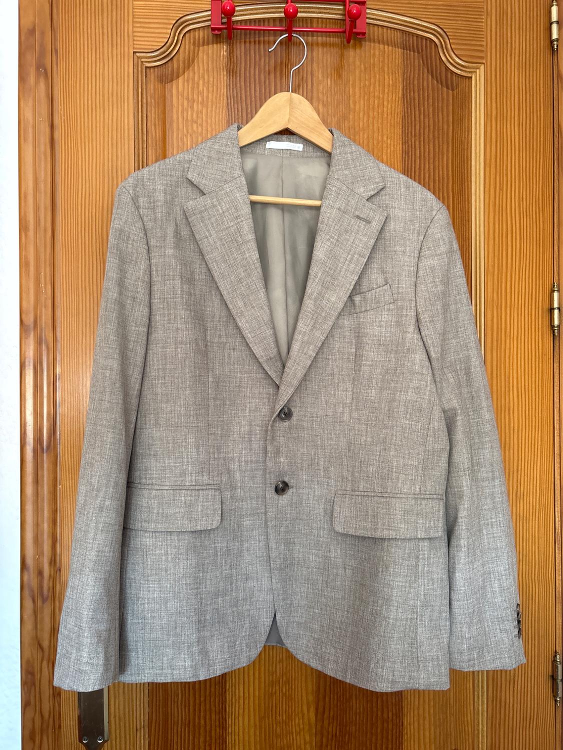 Grey suit jacket hanging on a wooden hanger over a wooden door. The jacket has two buttons and classic lapels.
