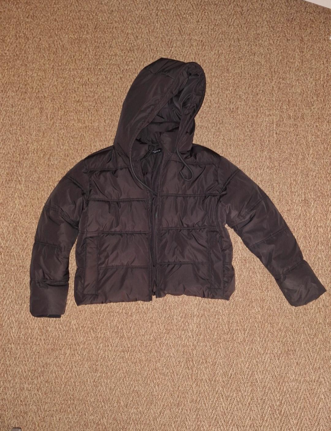 Brown padded jacket with a hood, placed on a beige rug. The jacket has a front zip fastening and long sleeves.