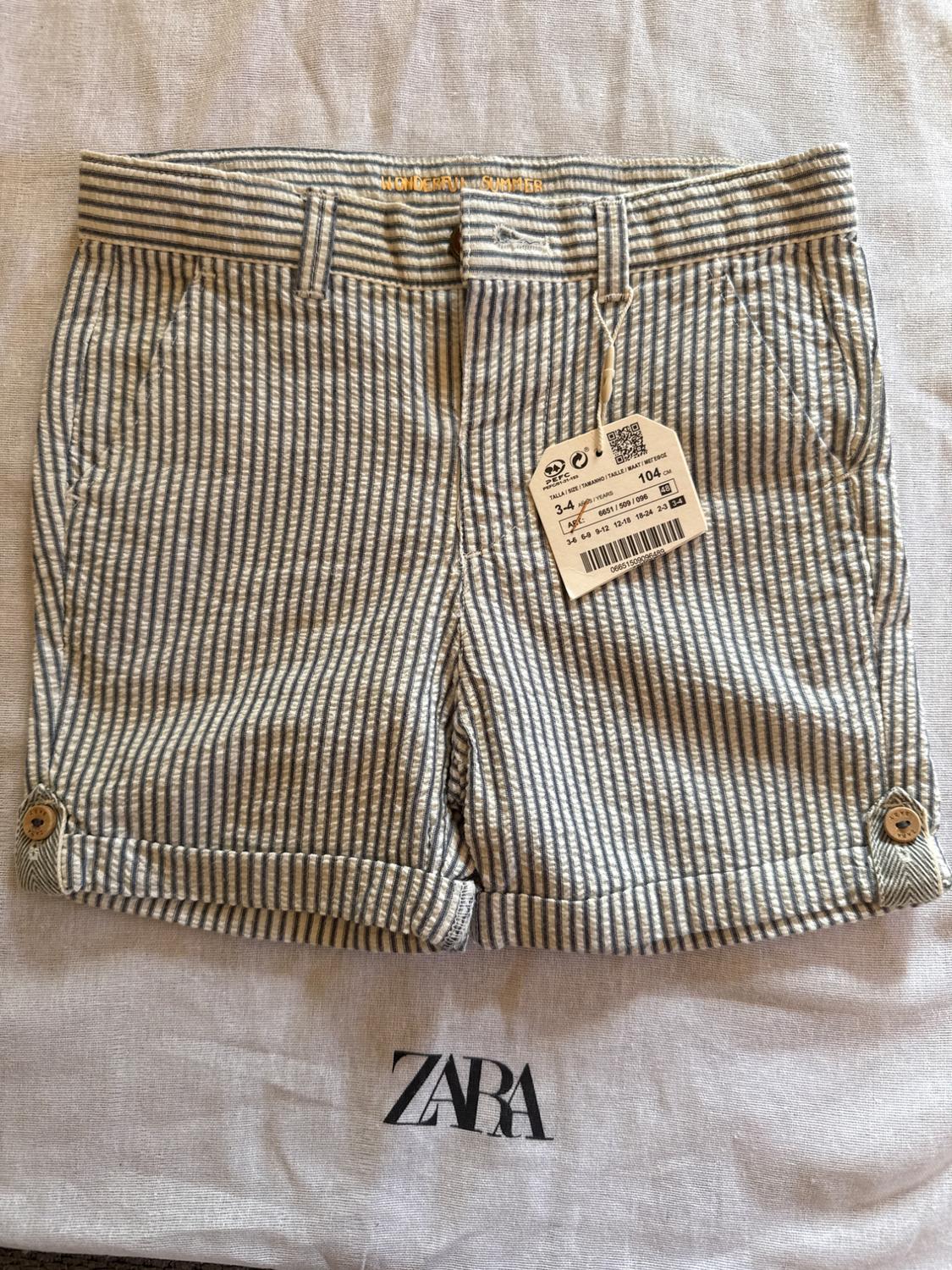 Gray and white striped shorts with tag, on fabric with Zara logo. Visible text: "WONDERFUL SUMMER". Size 3-4 years, 104 cm.