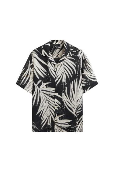 Short-sleeved shirt with white leaf print on a black background. Open collar and front buttons.