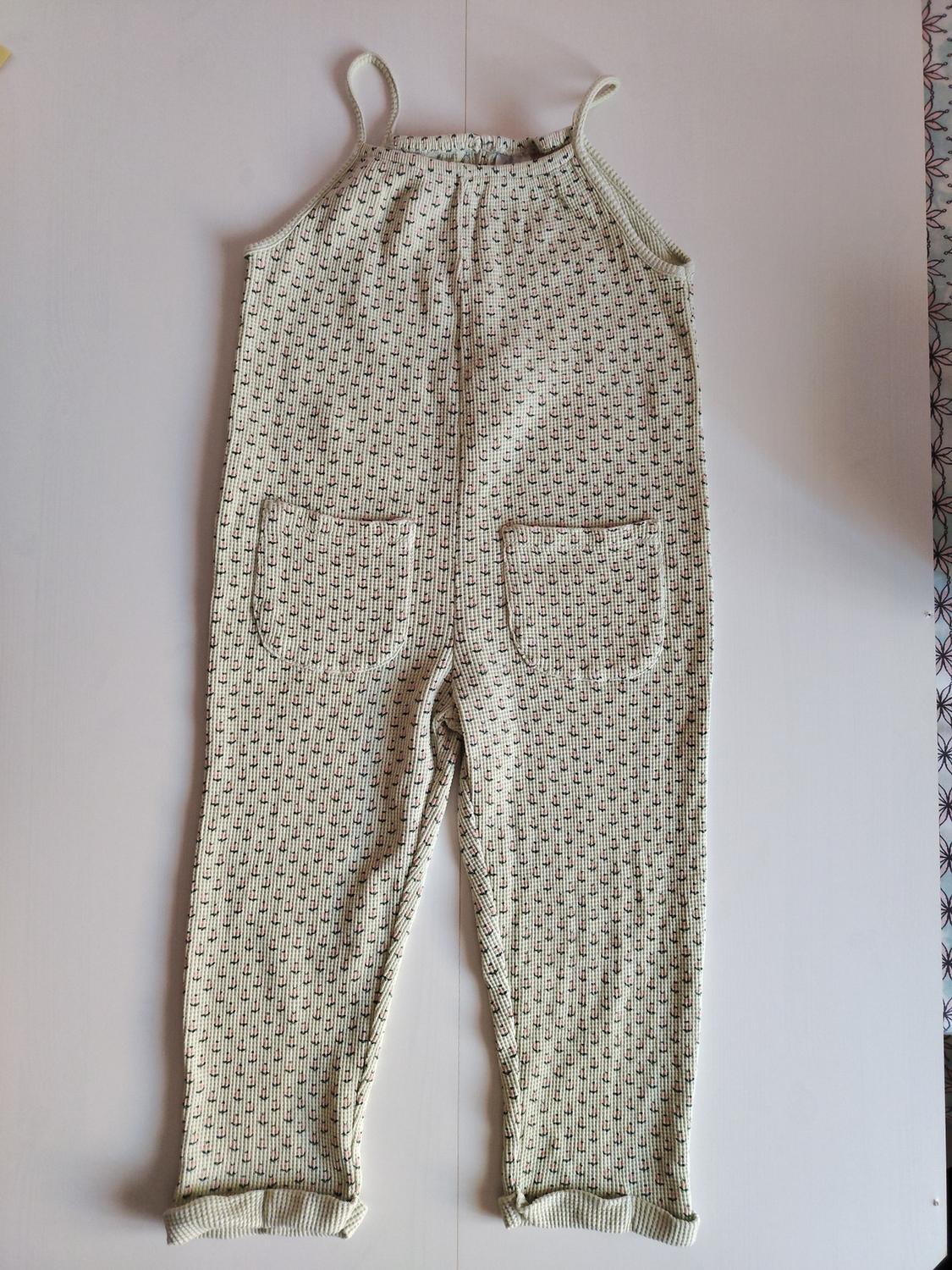 Dungarees with a geometric print in beige and black tones, front pockets and ankle cuffs, on a white background.