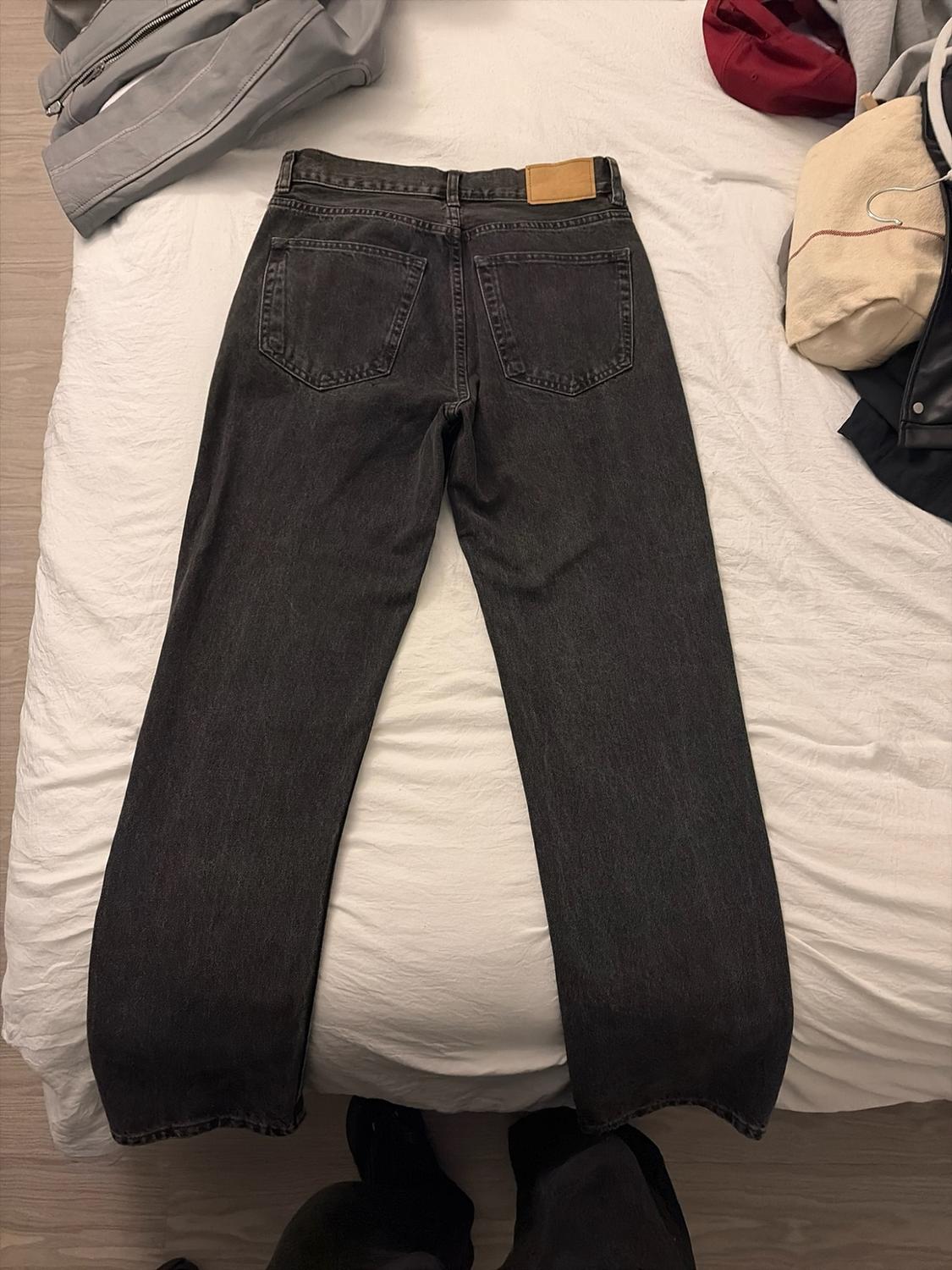 Black jeans seen from behind on a white bed. The pockets and a brown patch are visible in a casual setting with other clothing.