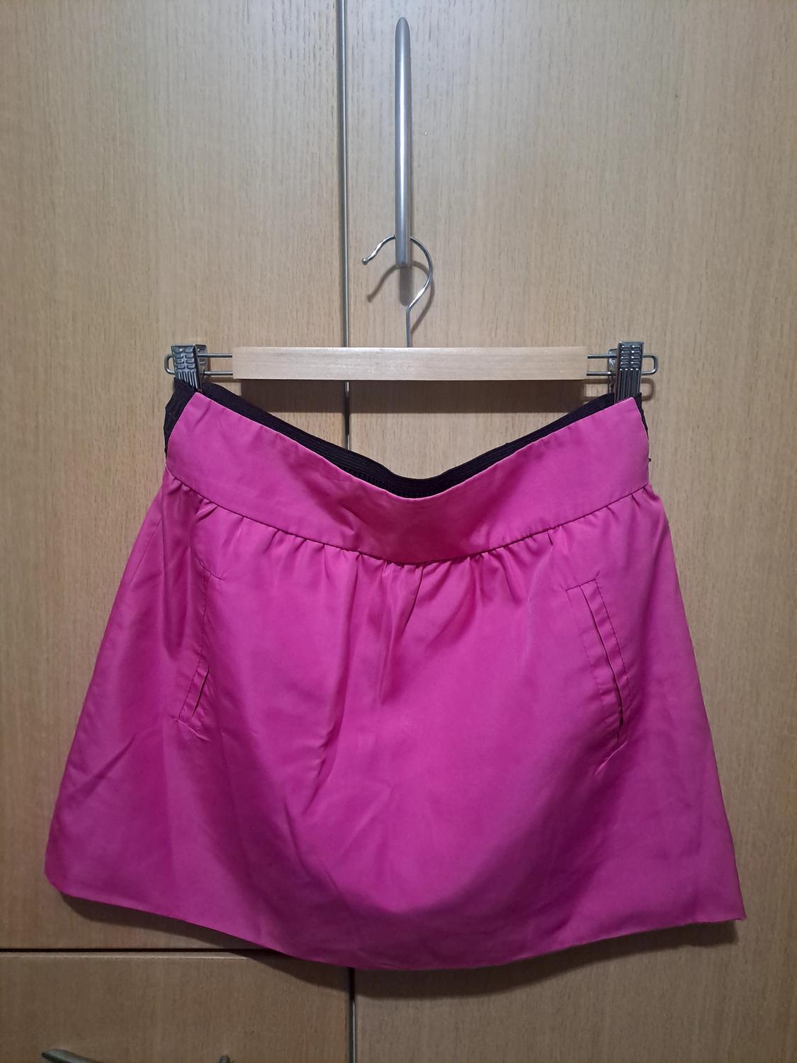 Pink mini skirt hanging on a wooden hanger against a light wood wardrobe background.
