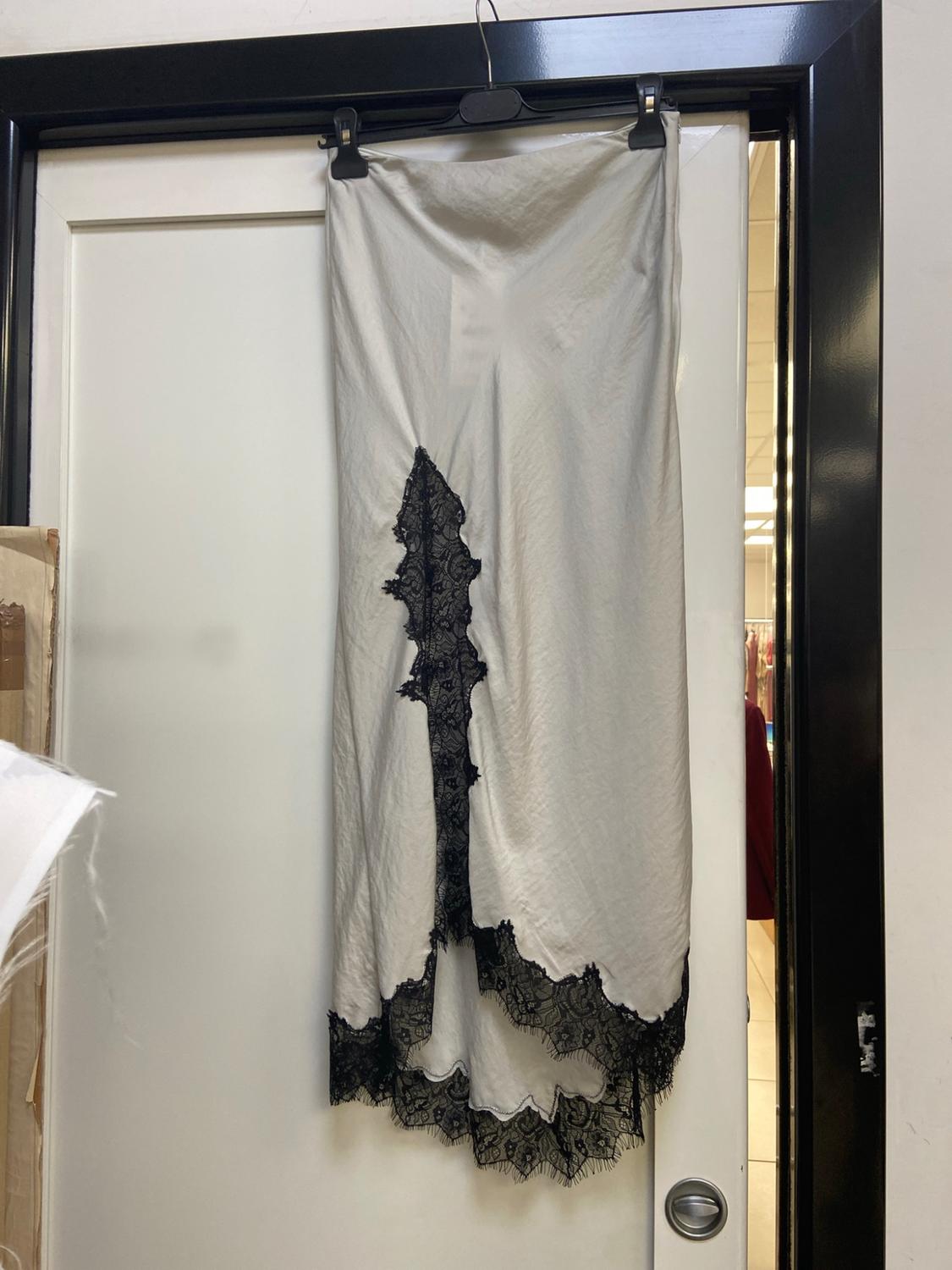 White slip skirt with black lace at the hem and a split, hanging from a hanger on a white door.