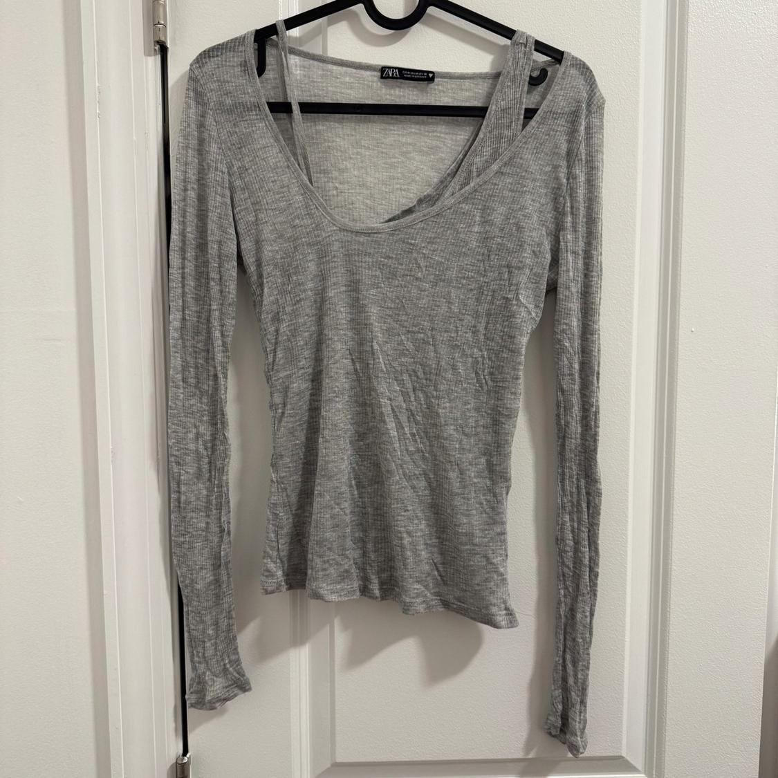Gray long-sleeved t-shirt hanging on a black hanger over a white door. Visible tag on the collar.