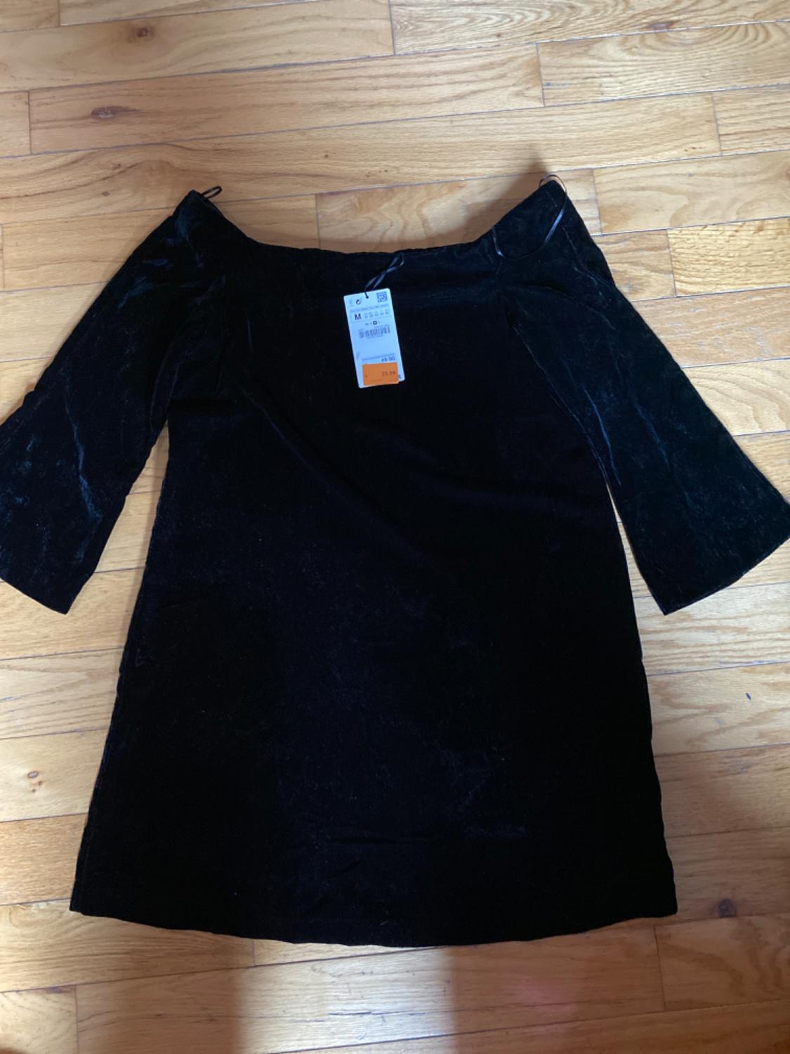 Front view of a black dress with three-quarter sleeves and a boat neckline, label visible in the center.