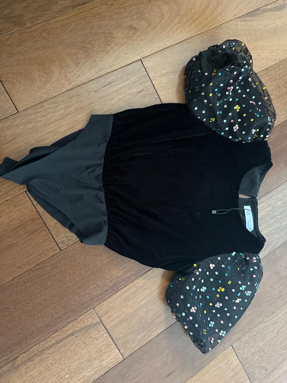 Black velvet bodysuit with puffed black tulle sleeves with colored sequins, on light wood floor.