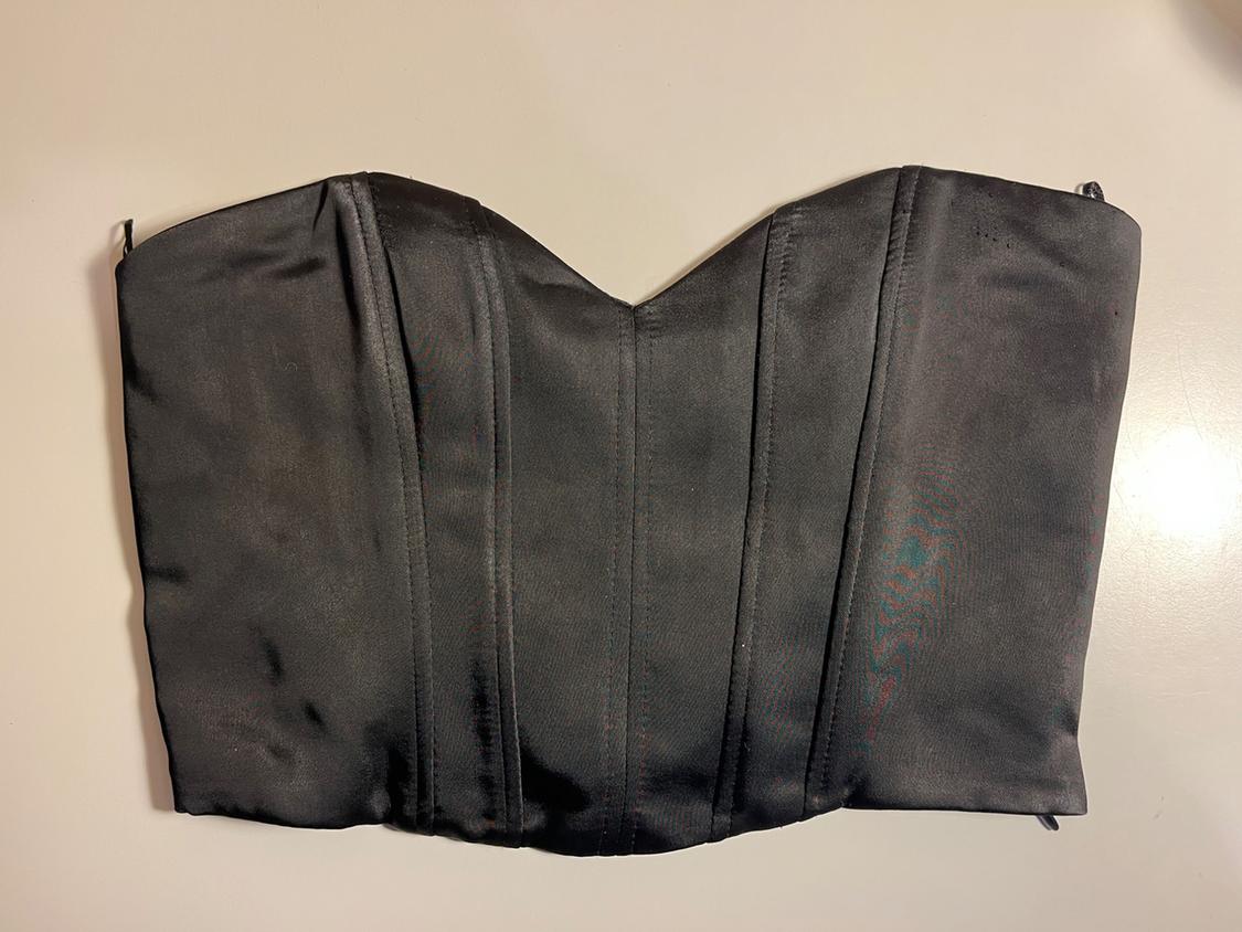 Black satin corset with vertical seams, on a white background. Elegant and structured design.
