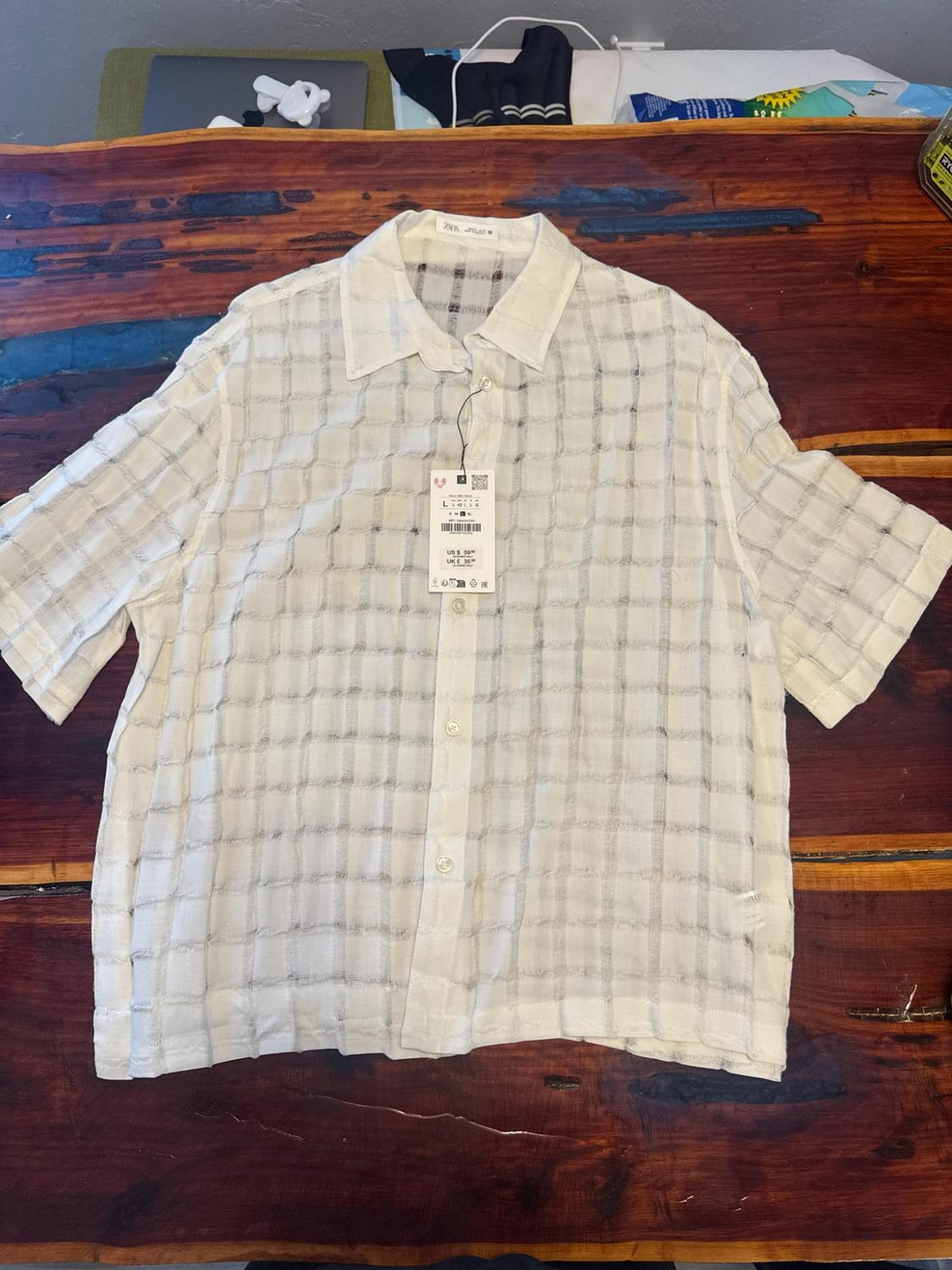White short-sleeved grid-pattern shirt on a wooden table. Label with text: ZARA L US $ 59.90 UK £ 35.99.